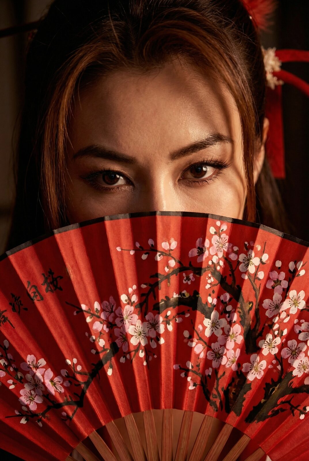 Eyes over the painted fan, direct, amused, unbothered. Japan finds her too bold — too confident, too open. The West files her under exotic. She stopped auditioning for either verdict years ago. Mai Shiranui taught her confidence; she’s just paying it forward — and the woman holding the fan is done letting anyone else hold the definition.
